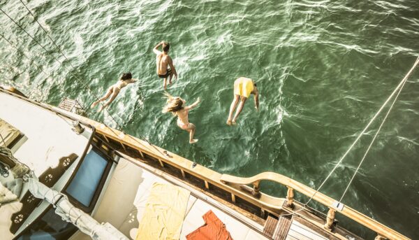 Aerial view of young people jumping from sailing boat on sea trip