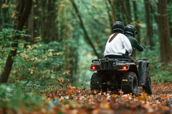 Driving on the footpath. Young couple riding a quad bike in the forest